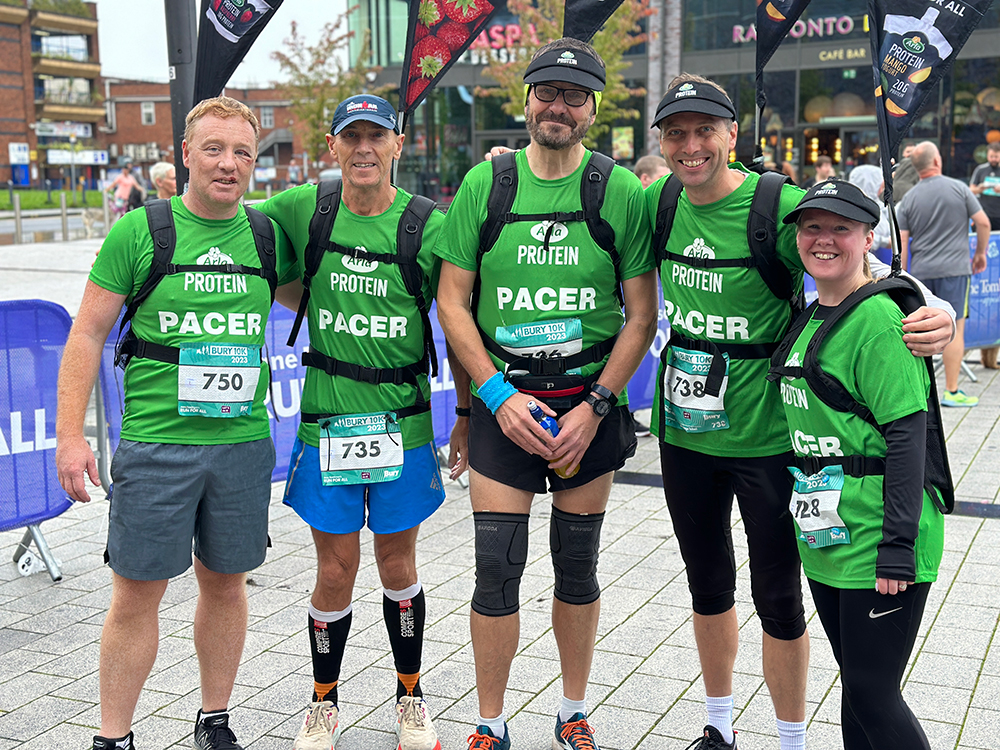 Four people standing in a row all wearing race numbers on their t-shirts