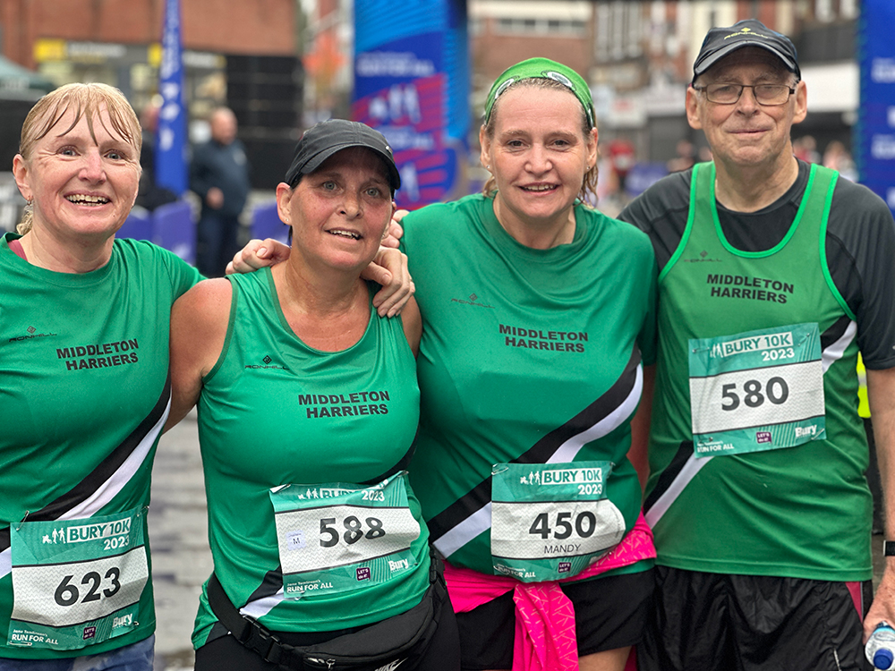 Four people standing in a row all wearing race numbers on their t-shirts