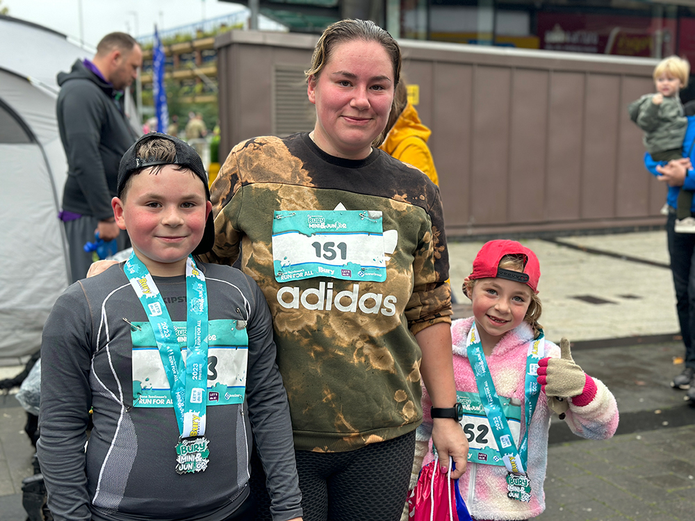 Two children wearing race medals standing with an adult