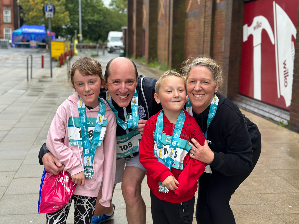 Two children wearing race medals standing with two adults