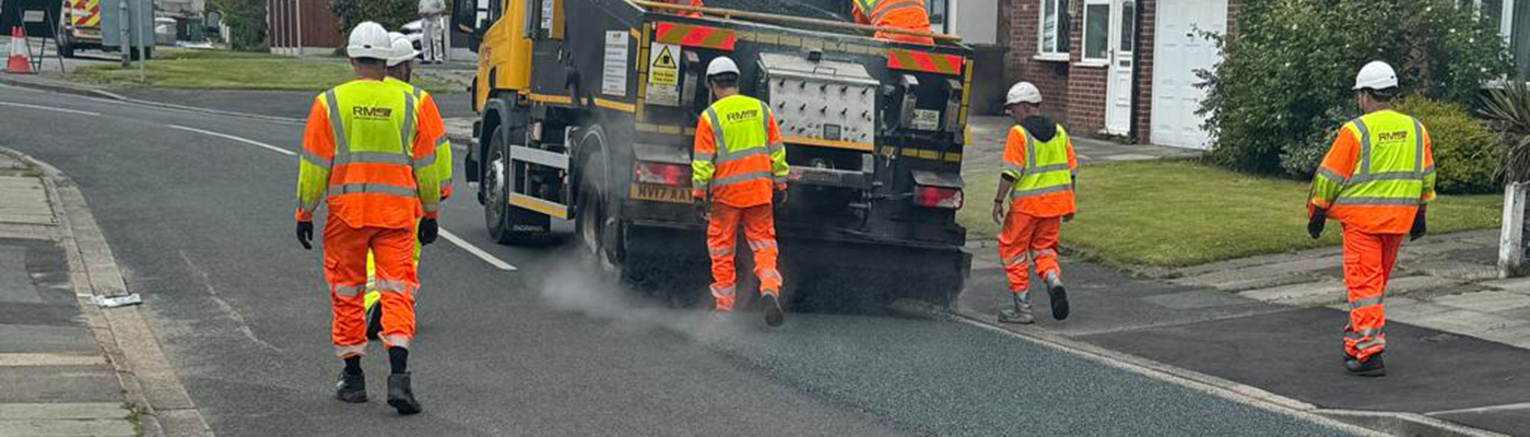People dressed in high-visibility clothing stood around a vehicle on a road