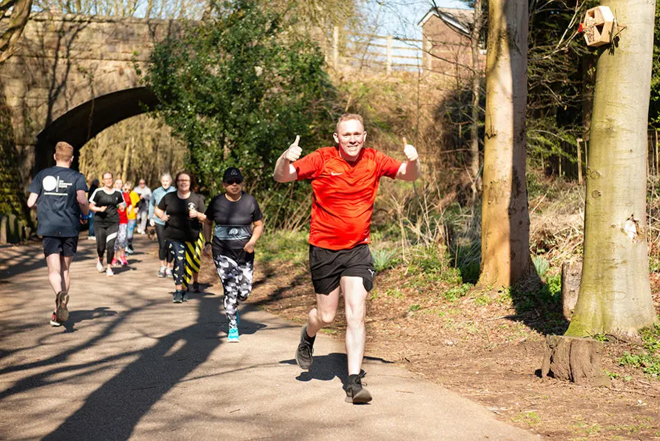 Man running on a countryside lane giving a thumbs up gesture