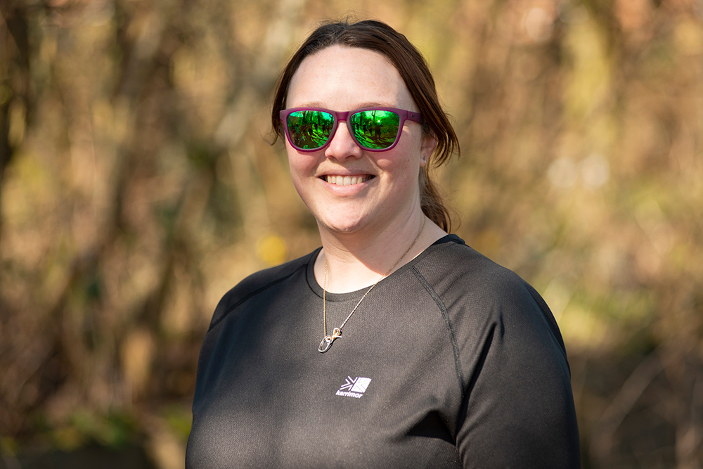 Smiling person wearing sunglasses and a black t-shirt with trees in the background