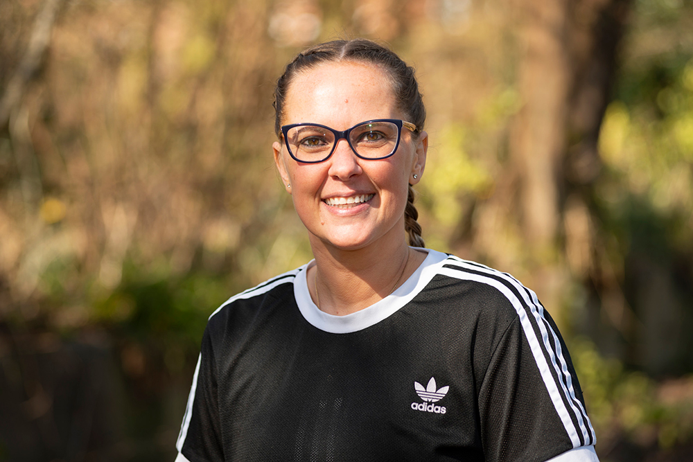 Smiling person wearing glasses and a navy t-shirt with trees in the background