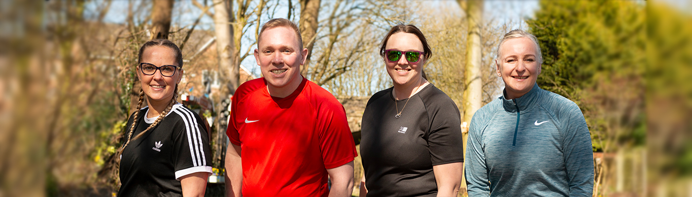 Four people wearing tshirts stood in line surrounded by trees