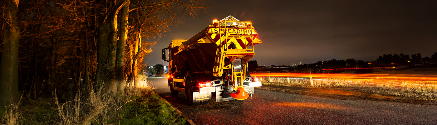 A gritting truck travelling along a road during the night-time