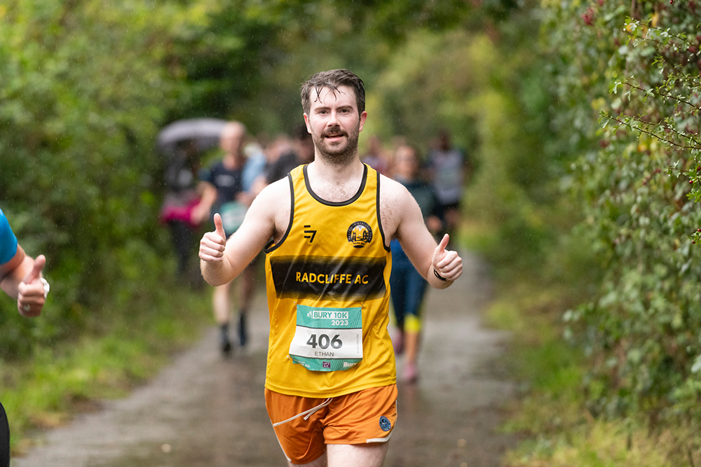 A person running on a countryside lane giving the thumbs up sign