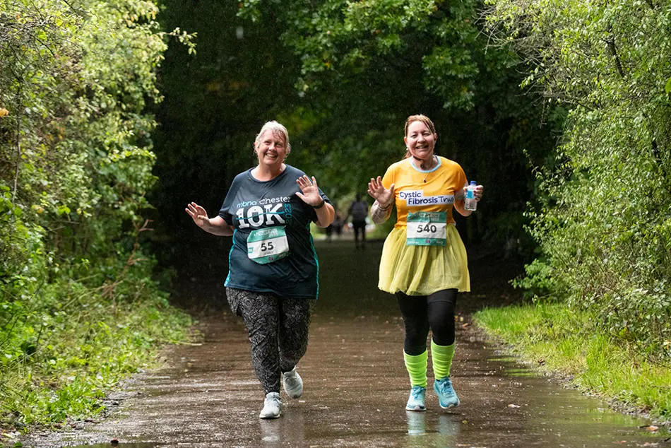 Two smiling people running on a countryside lane surrounded by trees