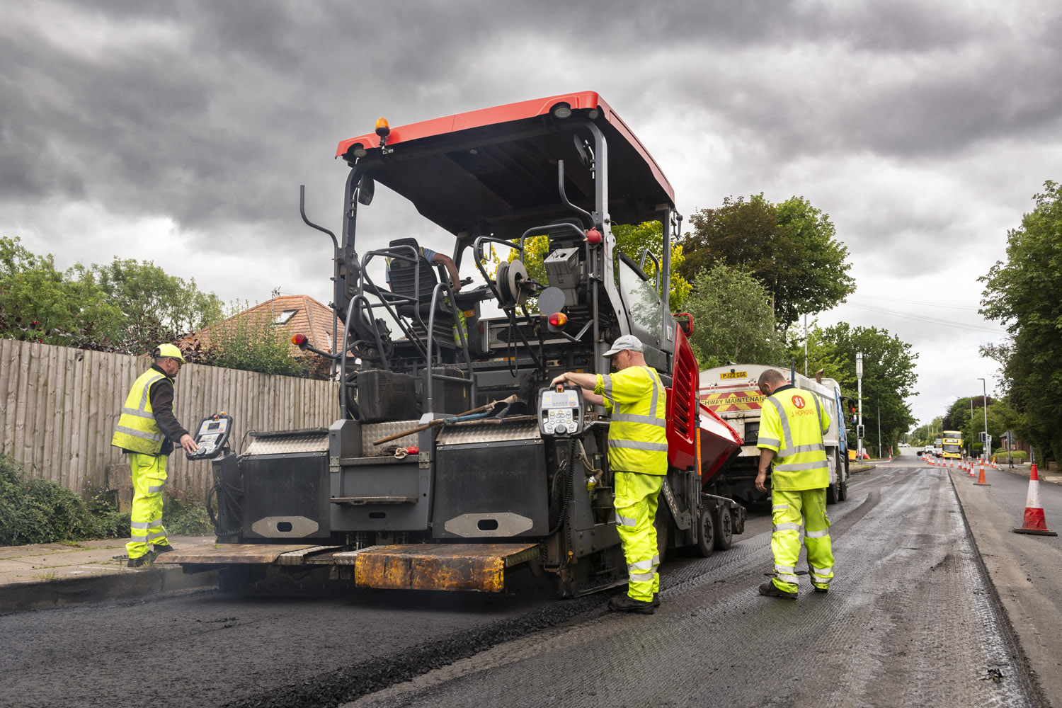 A group of people in high-visibility clothing using a large machine to lay tarmac onto a road surface