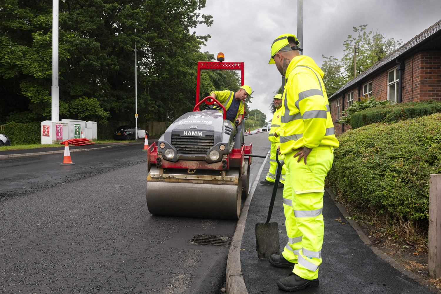 A person wearing high-visibility clothes watching a machine that is rolling along a road surface