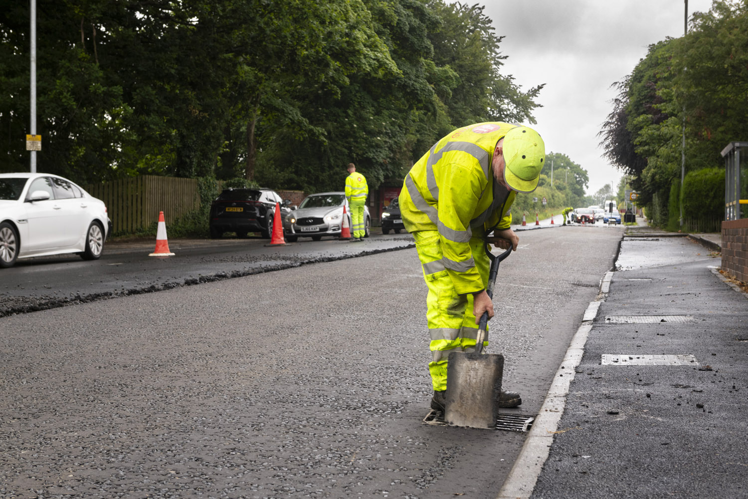 A person wearing high-visibility clothes using a spade on a road surface