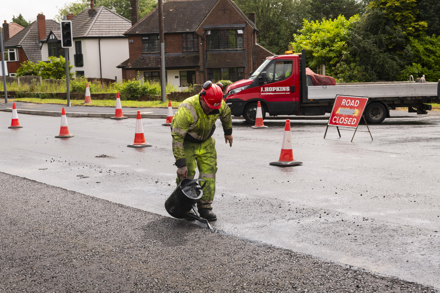 A person wearing high-visibility clothes pouring water from a can onto a road surface