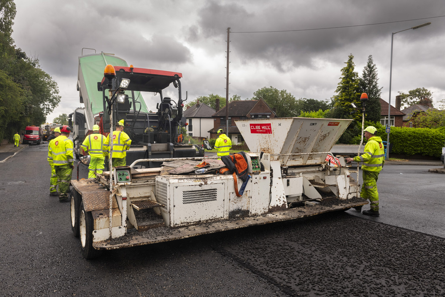 A group of people in high-visibility clothing using a large machine to lay tarmac onto a road surface