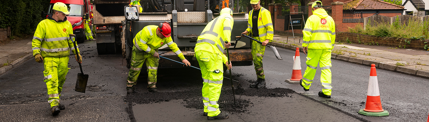 A group of people in high-visibility clothes standing around a machine that is placing tarmac onto a road surface