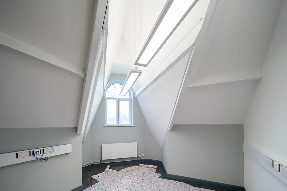 A long empty room with plain walls. There is an arch-shaped window at one end