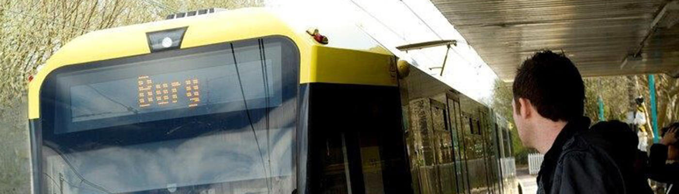 A person stood on a platform next to a yellow tram with the word 'Bury' on the front