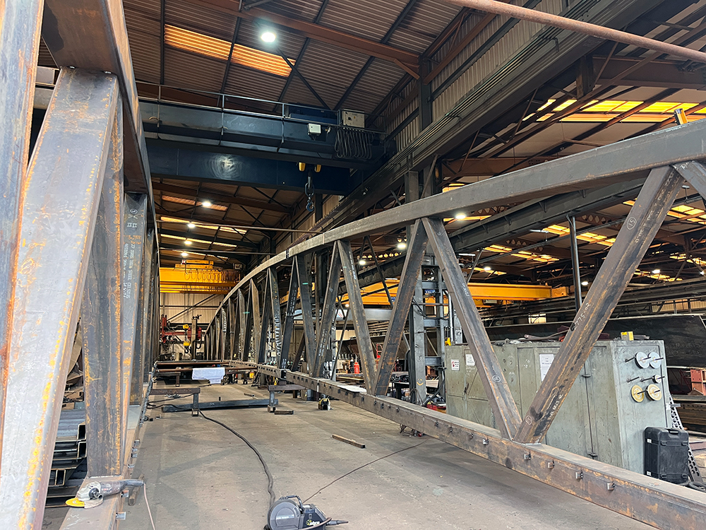 A large metal bridge under construction in a large warehouse