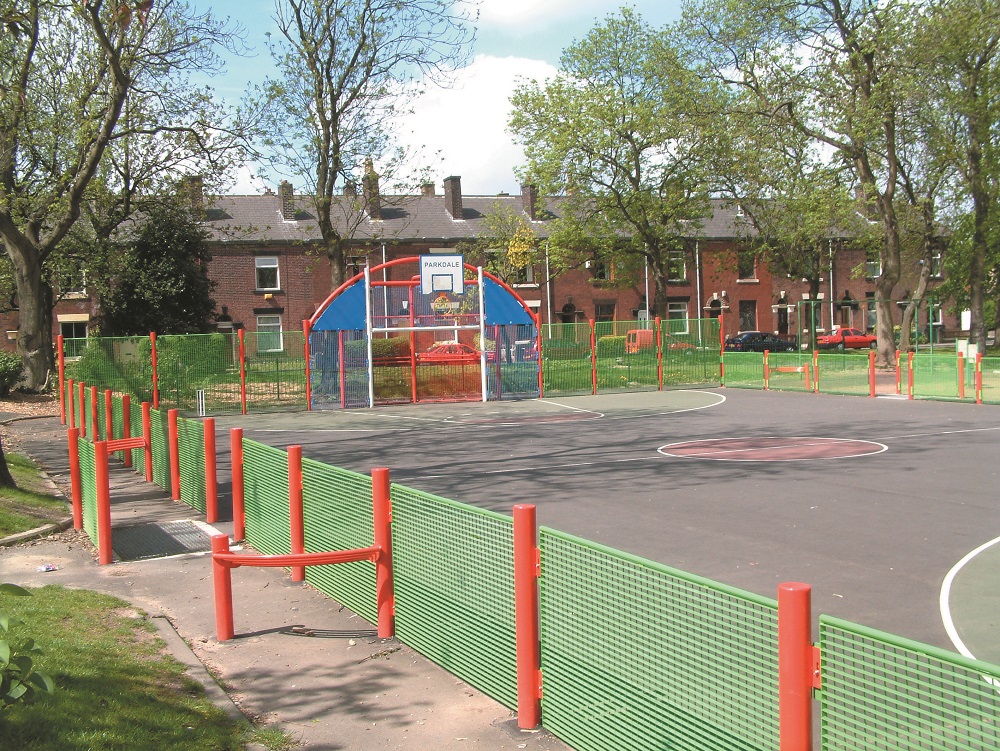 Gated ball playing area by trees and houses.