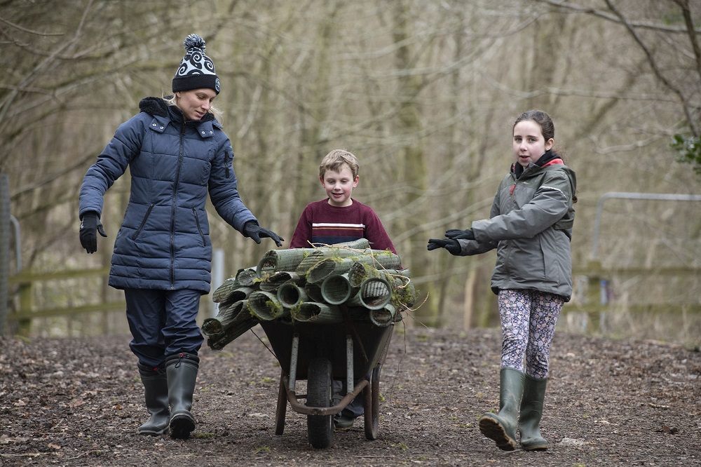 Three people pushing a full wheelbarrow.