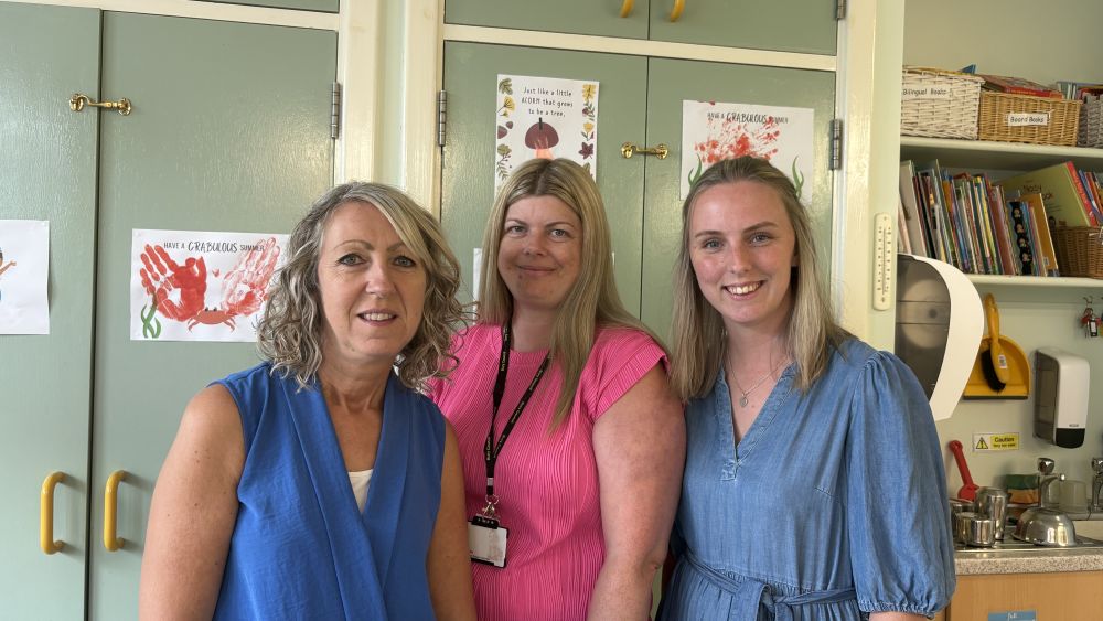 Three ladies stood in an office smiling into the camera.