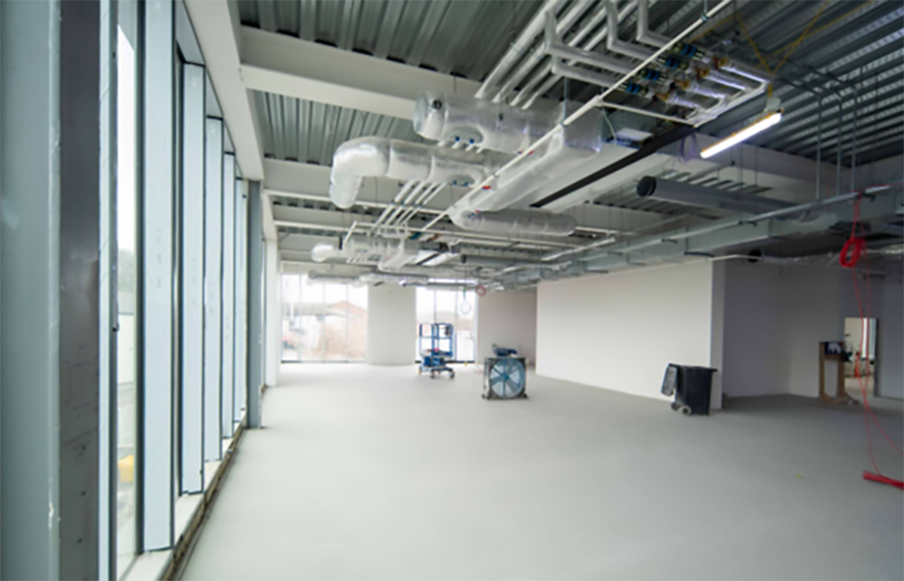A large empty room with floor to ceiling windows and exposed pipework on the ceiling
