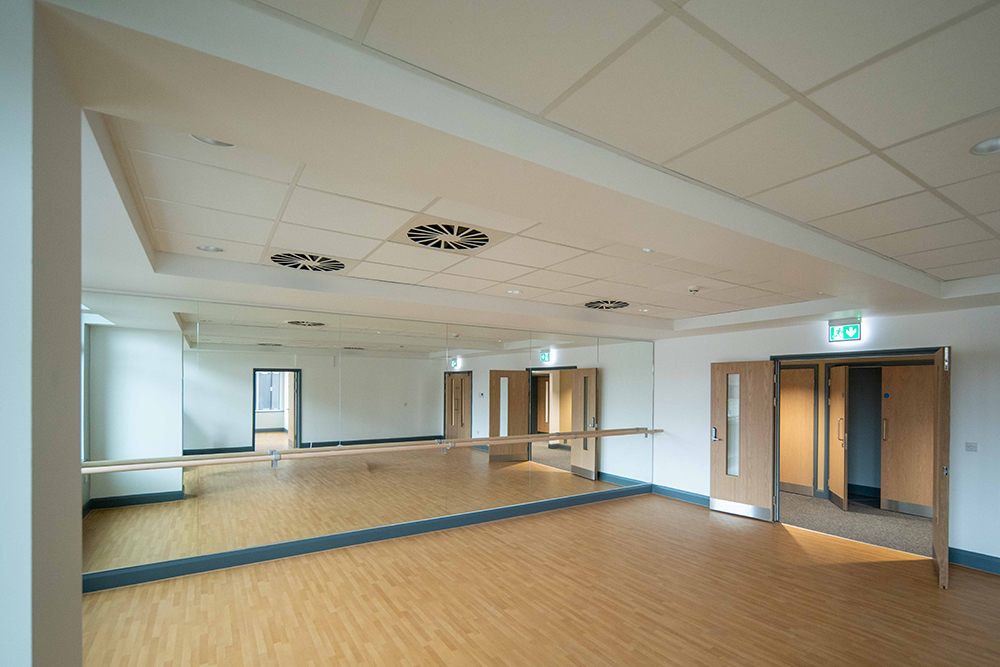 A large empty room with a wooden floor and a mirror wall on one side