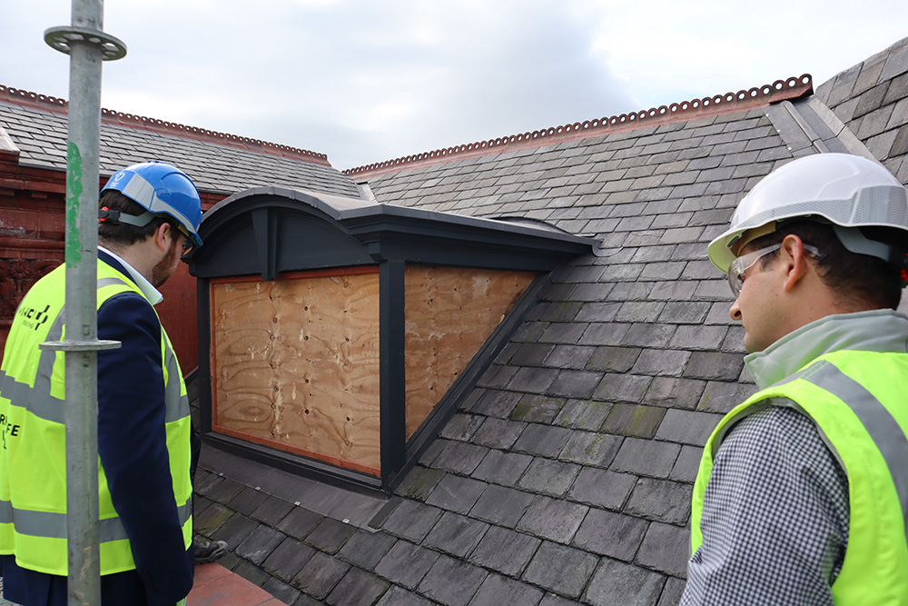 Two people dressed in safety clothing looking at a slate roof on a building