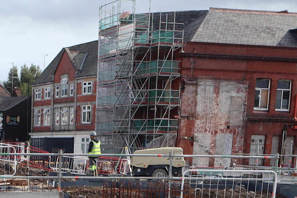 A red brick building with scaffolding covering one wall behind a construction site