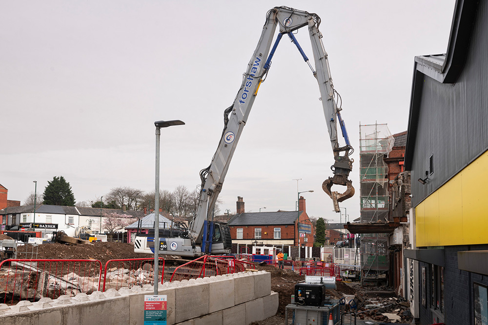 A large crane on a building site removing part of the outside of a building