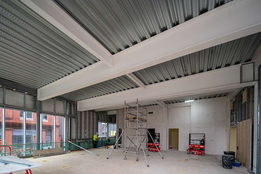 An empty room with large windows along one side. There are construction materials across the floor 