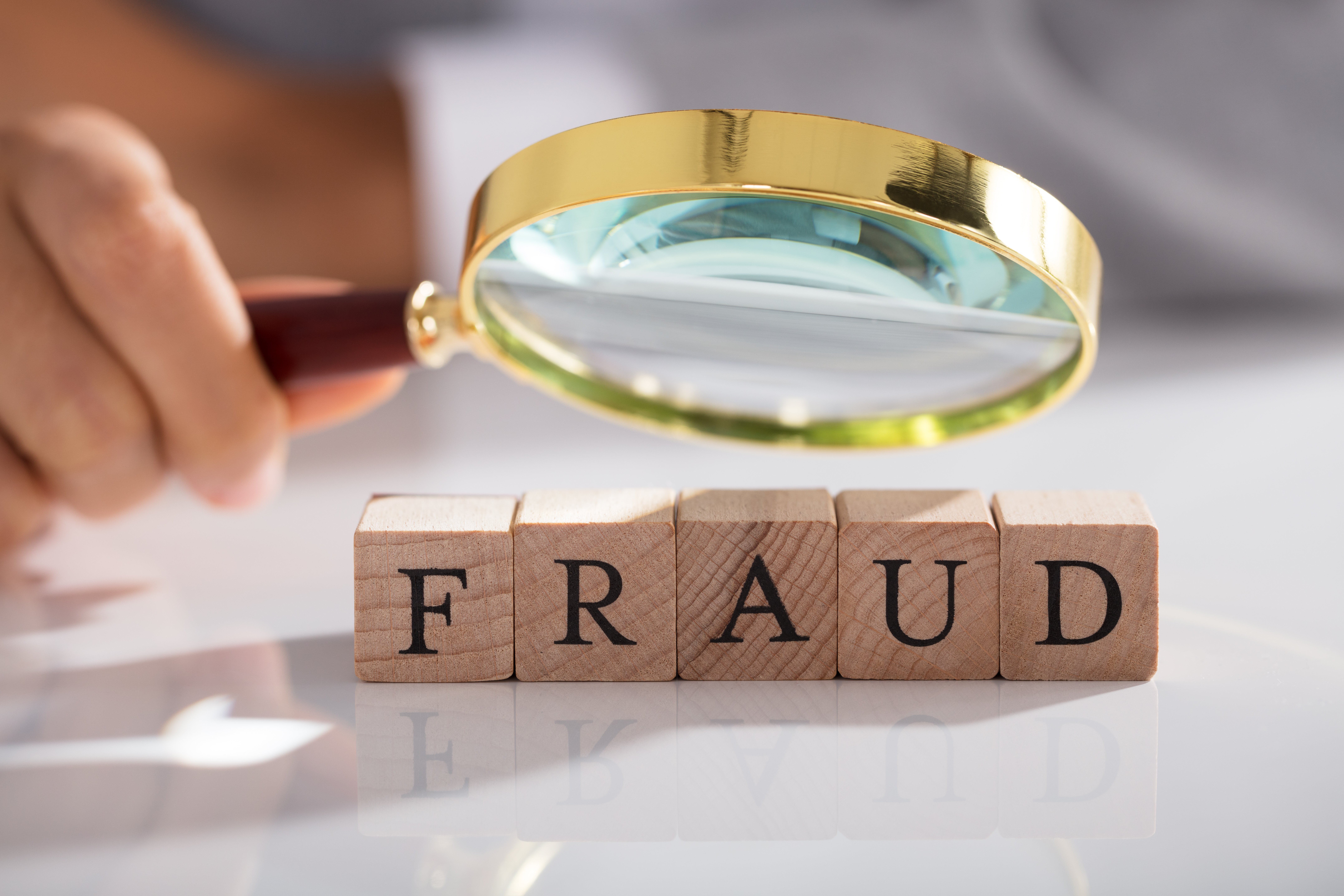 Magnifying glass pointed at wooden blocks that spell FRAUD 