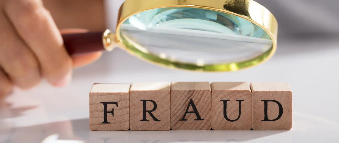 Magnifying glass pointed at wooden blocks that spell FRAUD