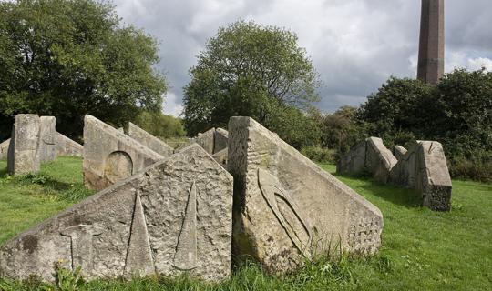 Large stones on a field with chimney in background.