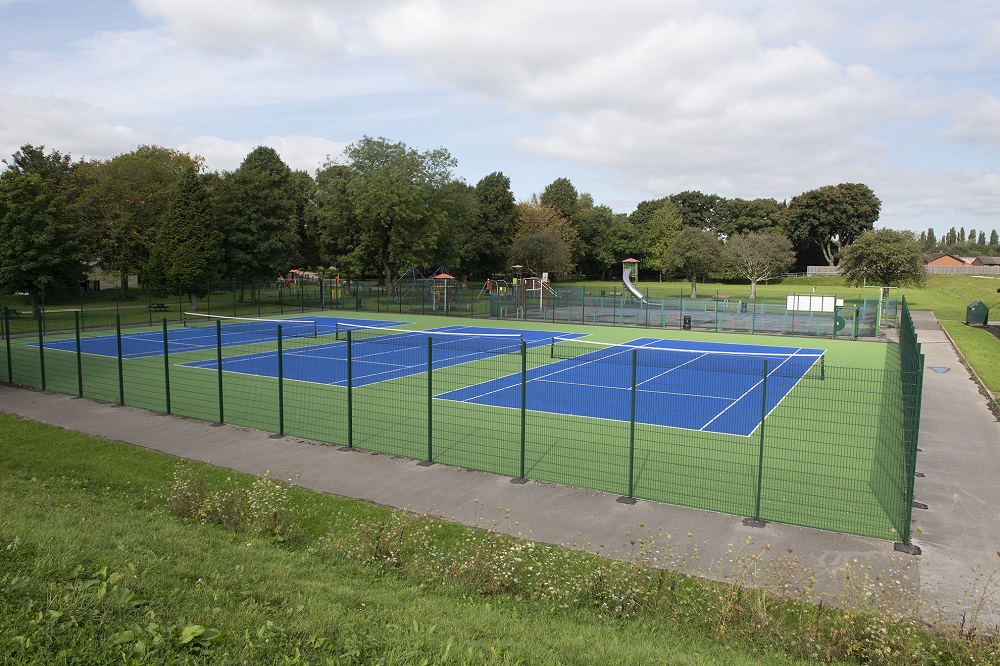 Fenced off blue surfaced tennis courts.