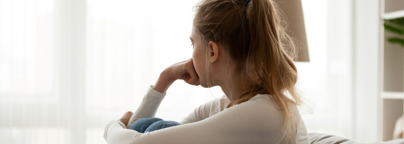 A young person hugging their knees to their chest looking worried