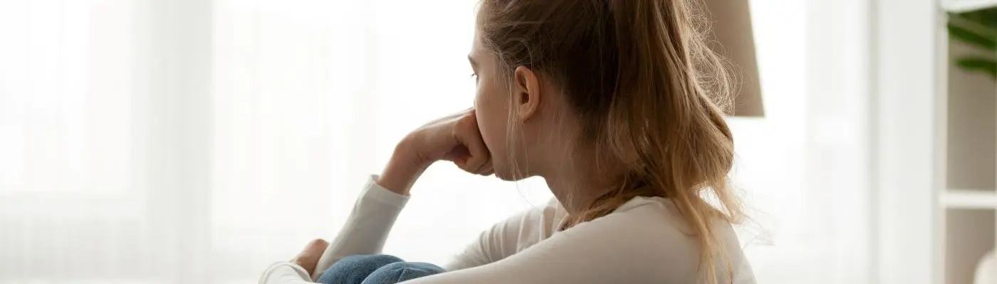 A young person hugging their knees to their chest looking worried