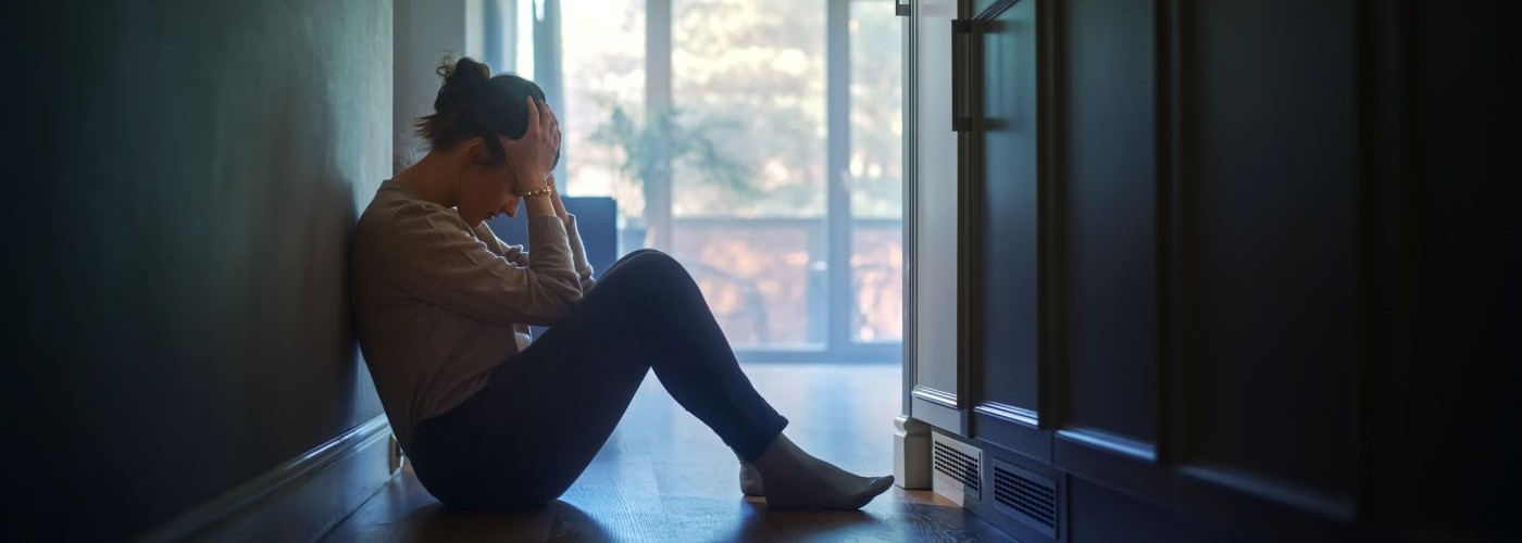 woman sat on floor in dark room holding head in her hands
