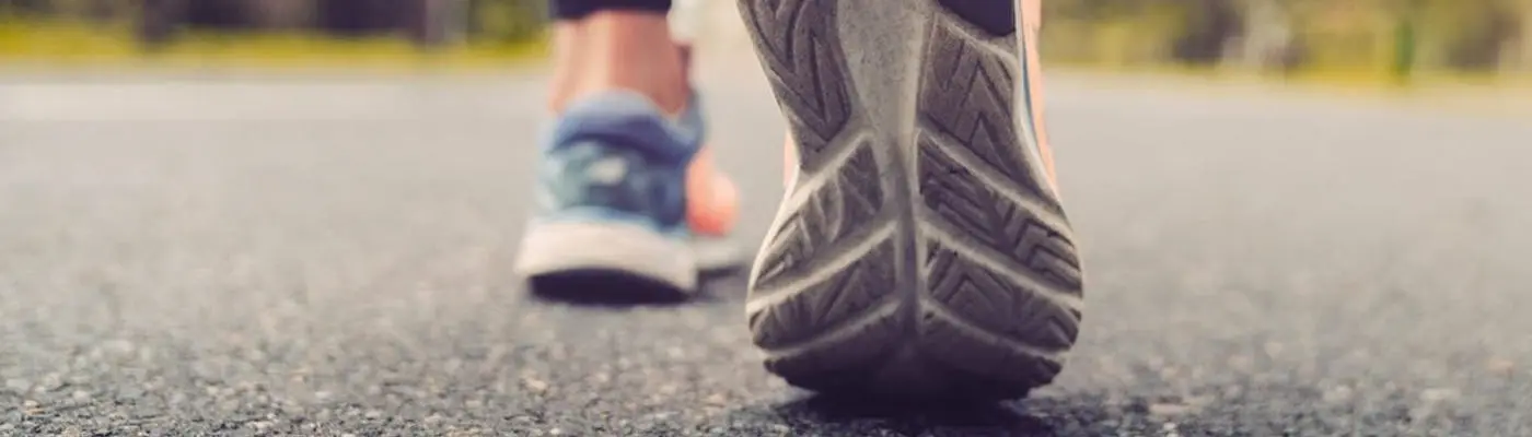 A pair of feet in training shoes walking on a path