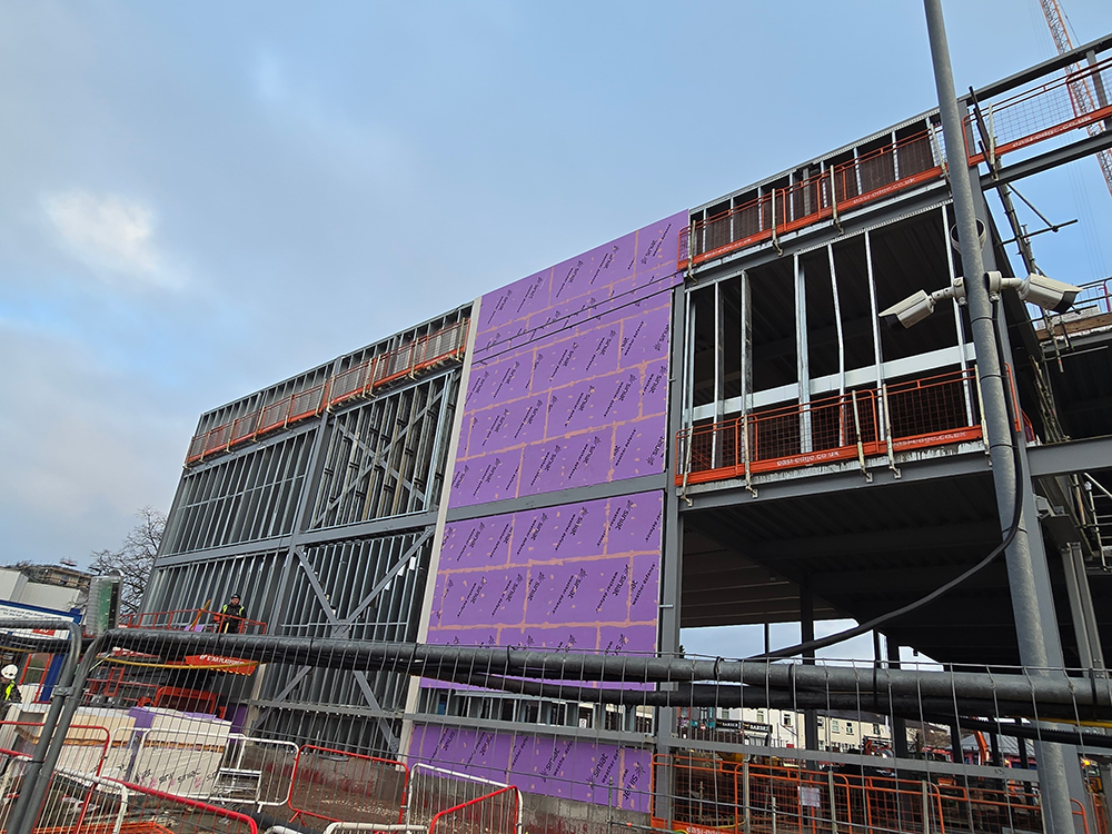 A steel frame partly covered with a weather defence board on the side of a building that is being constructed