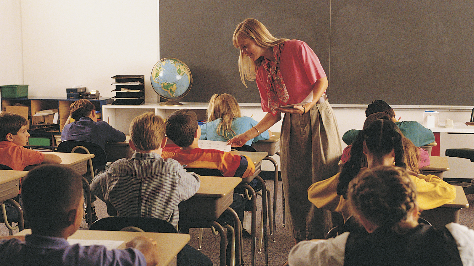 teacher handing out papers to children in a classroom