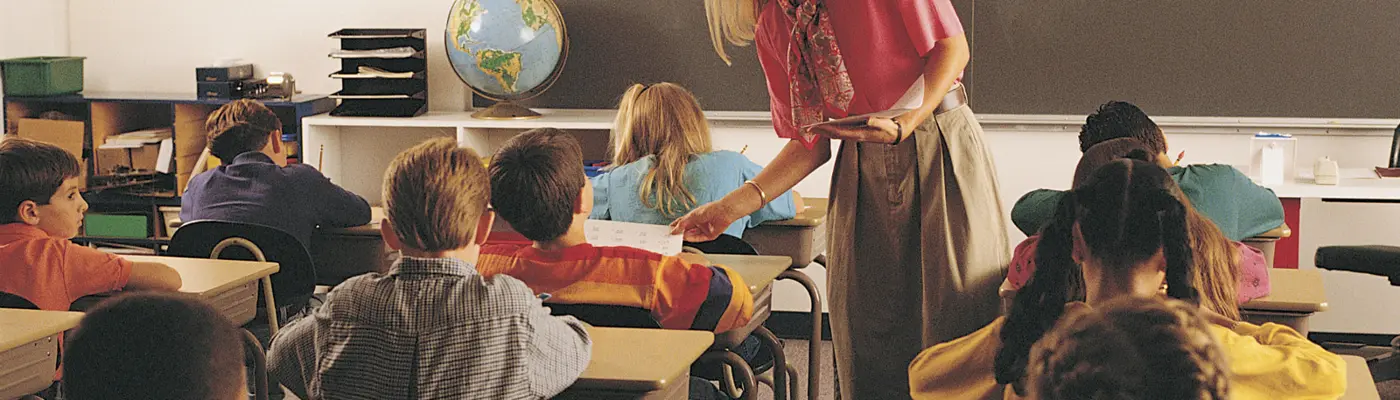 teacher handing out papers to children in a classroom