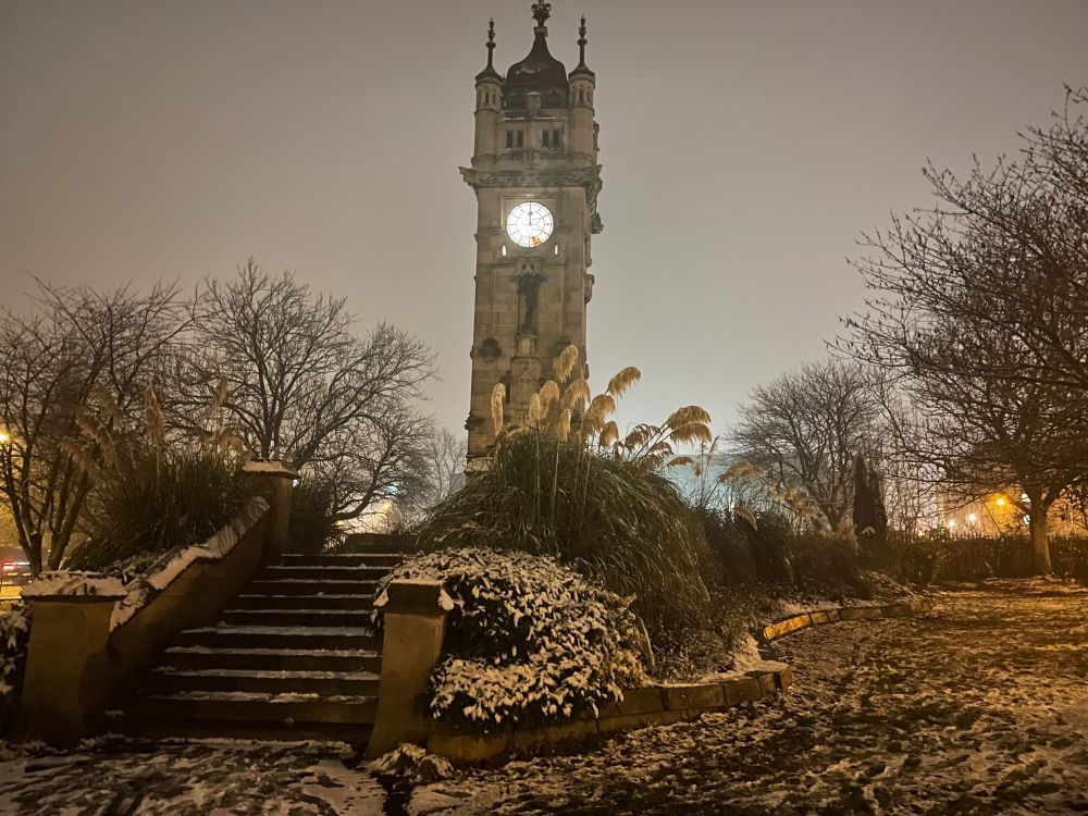 A large stone clock tower at dusk in the snow.