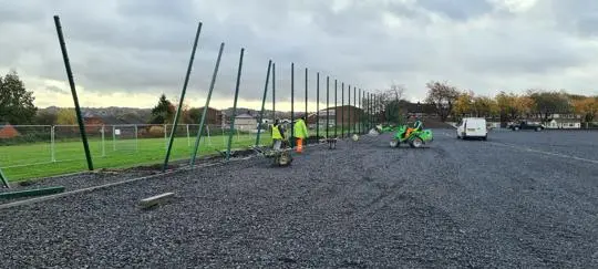 People in high-viz clothes erecting a high fence on a playing field