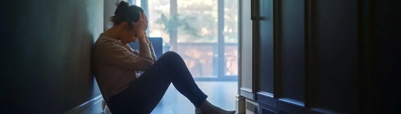 woman sat on floor in dark room holding head in her hands